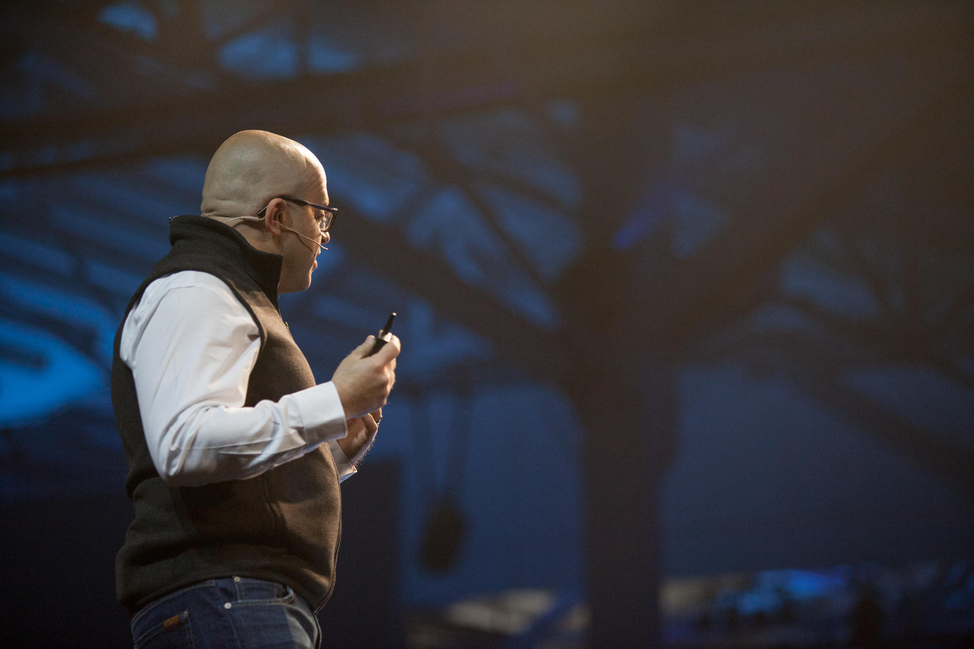 Close-up of speaker in vest presenting with moody blue theatrical stage backdrop